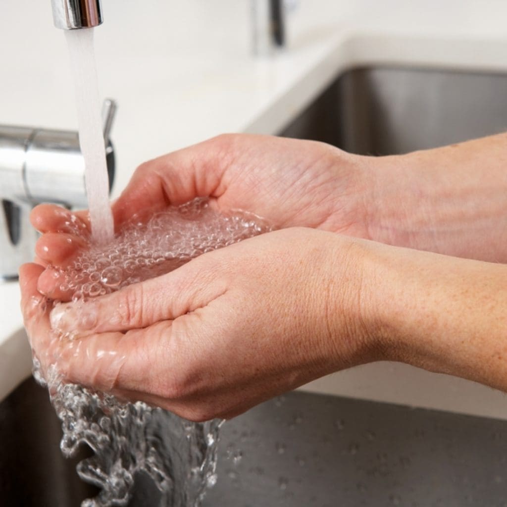 Someone washing hands in a sink to help illustrate healthy plumbing and water heater recirculation pump