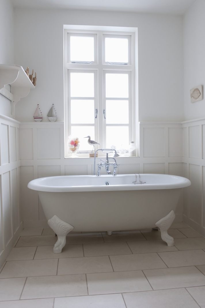 A newly remodeled bathroom featuring a white claw foot tub under a window letting in light to help illustrate remodel bathroom for airbnb includes using eco friendly fixtures you can then advertise online
