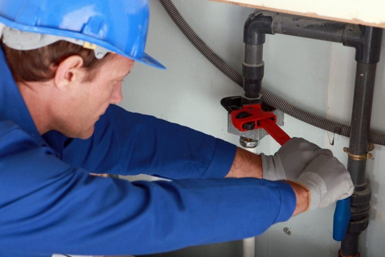 A plumber uses a wrench to check a water pipe to help illustrate how to know if you have polybutylene pipe and where to look for it