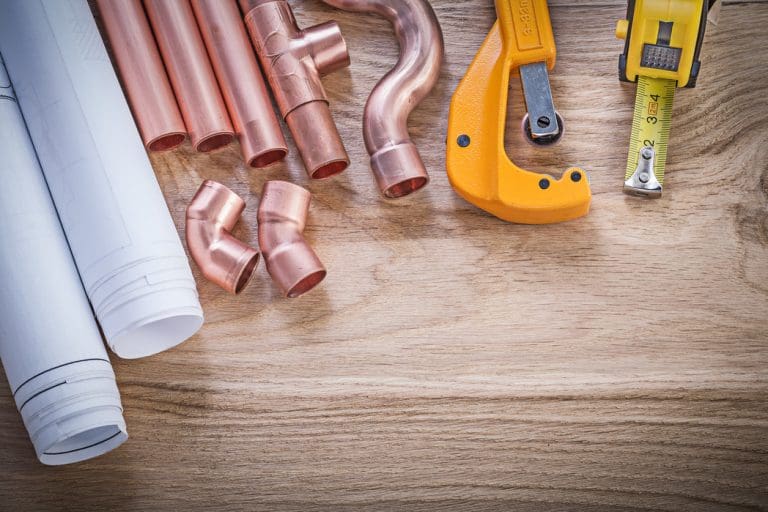 Copper pipe fittings and plumbing tools laid out on a workbench to help illustrate how Meticulous Plumbing handles a galvanized pipe replacement