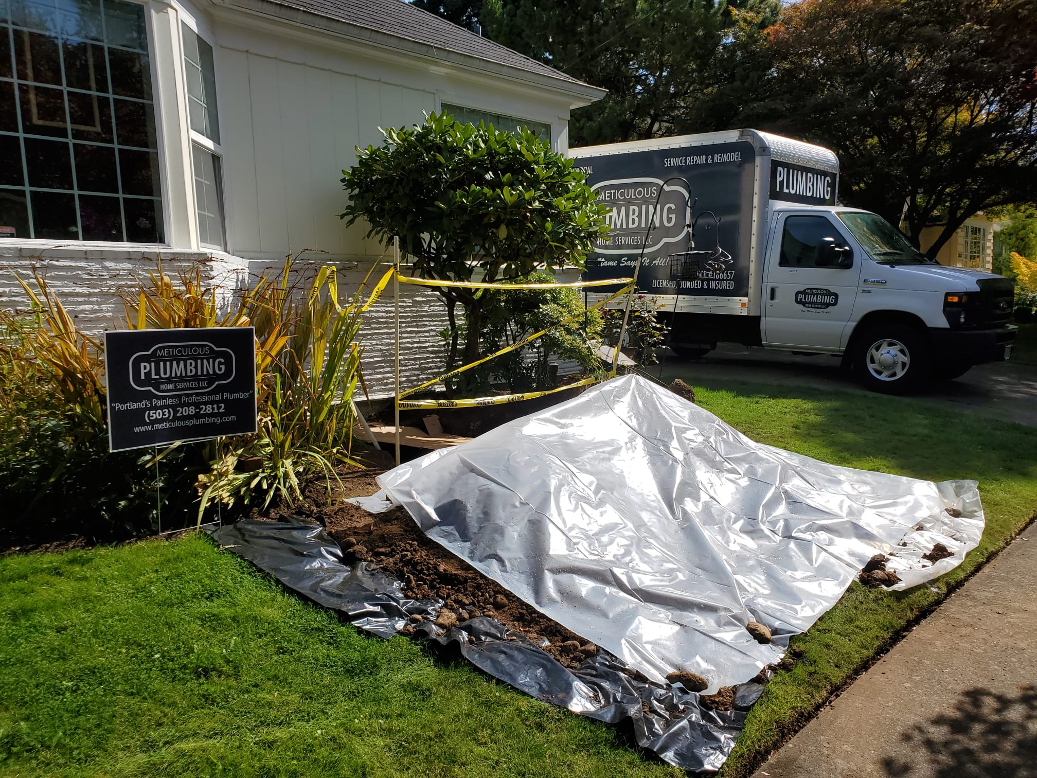 A large section of the lawn is covered by tarps and what looks to be a pile of dirt and a Meticulous Plumbing truck in the background to help illustrate main water line to house is leaking