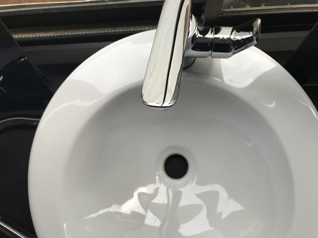 Modern bathroom faucet over a clean, round, ,white bathroom sink to help illustrate How to Deal With a Slow Bathroom Sink Drain