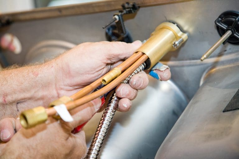 A plumber's hands working on kitchen faucet connections to help illustrate what happens when Meticulous Plumbing comes out