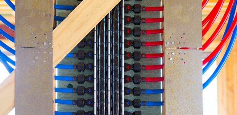 Blue and red PEX tubing connected to a manifold system for whole-home water distribution to help illustrate what happens during a repipe to replace polybutylene pipe