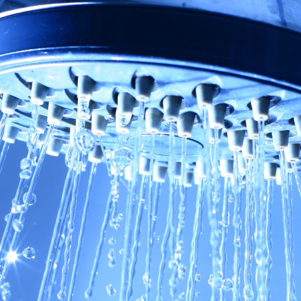 Closeup of a shower head against a blue background to help illustrate how to choose the right water heater and Reasons for Low Water Pressure