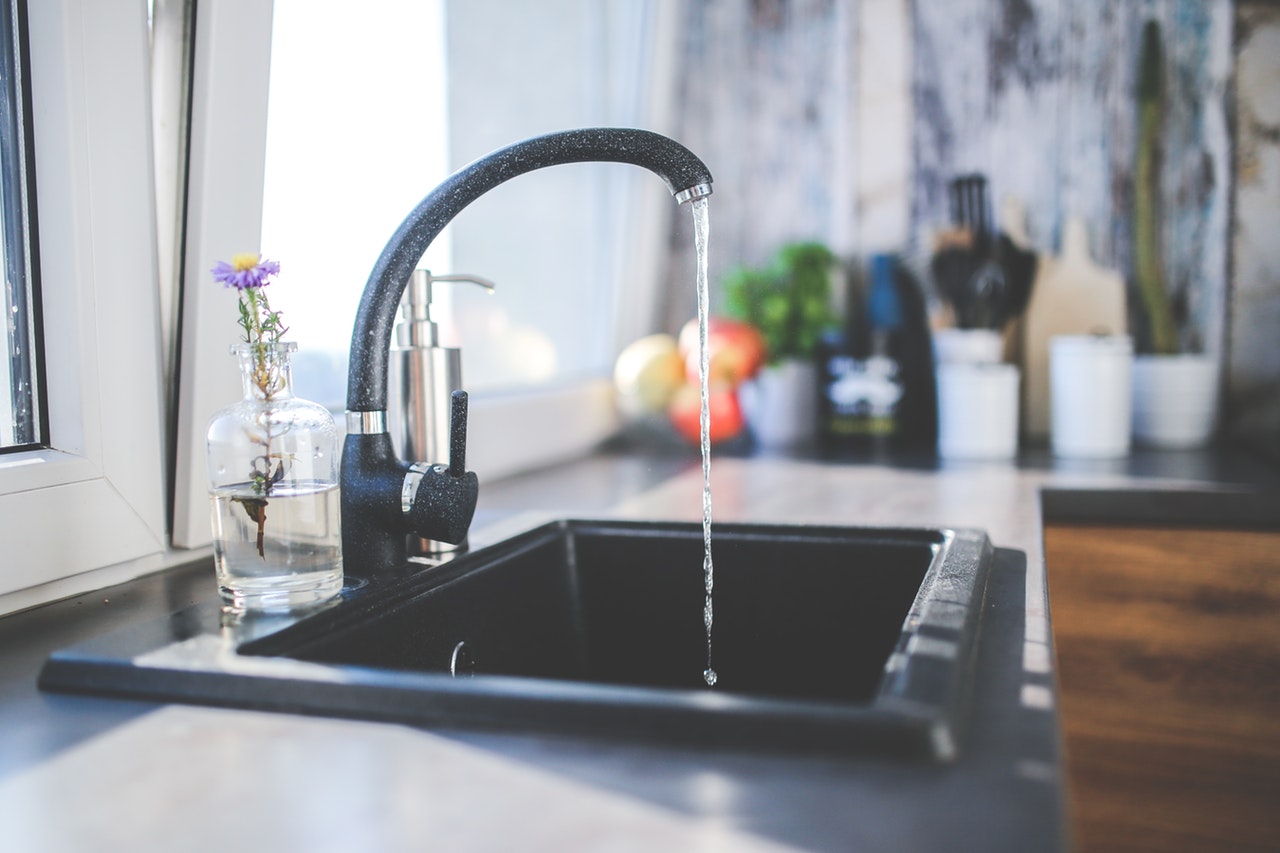 image of a kitchen faucet with water coming out to illustrate Cleaning a Drain With Baking Soda and Vinegar and whole home repipe.