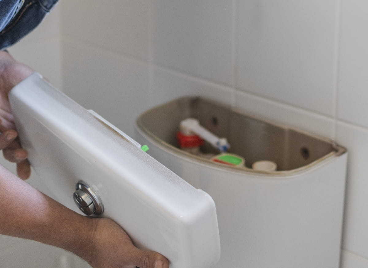 Plumber looking into the top of a toilet tank with top removed
