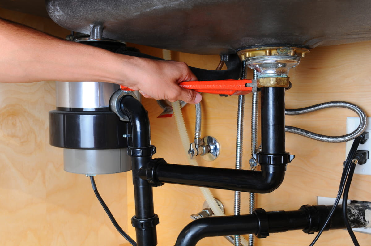 Closeup of a plumber using a wrench to tighten a fitting beneath a kitchen sink to help illustrate garbage disposal installation