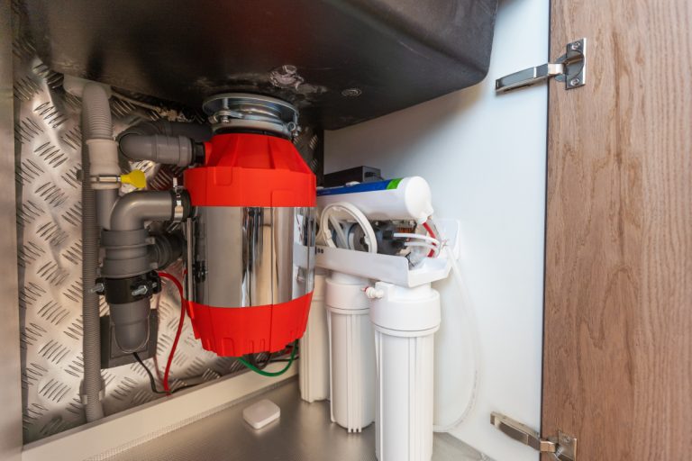A red garbage disposal installed in a kitchen sink cabinet to help illustrate whether to replace or keep your old disposal during a kitchen remodel