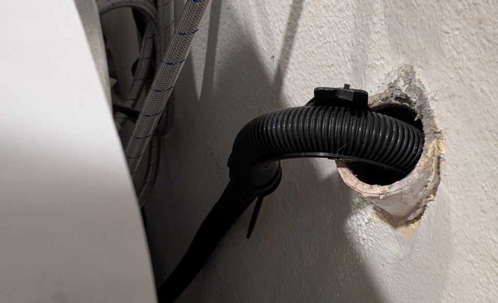 Image of a washing machine drain line going into the wall to help illustrate Plumbing a Washing Machine Drain