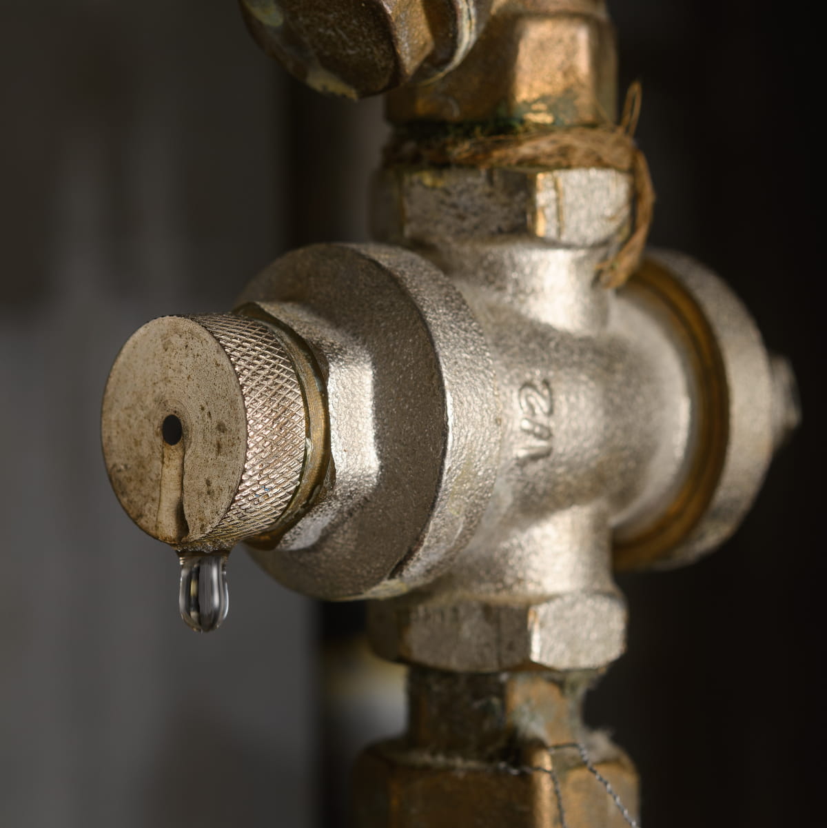 Leaking water pressure regulator on metal pipe in dark utility room signals water pressure regulator replacement